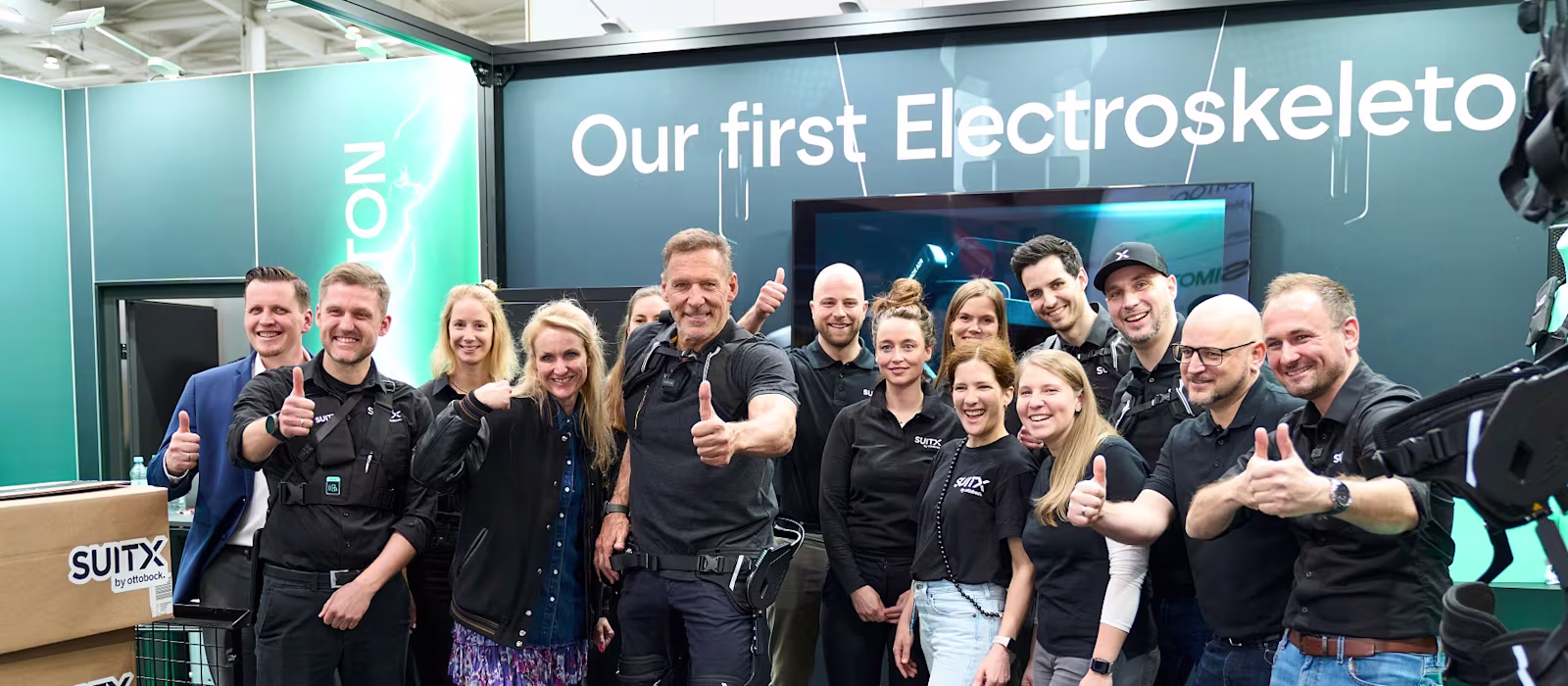 Eine Gruppe Menschen und Ralf Möller präsentieren den Hannover Messe Stand von SUITX by Ottobock.