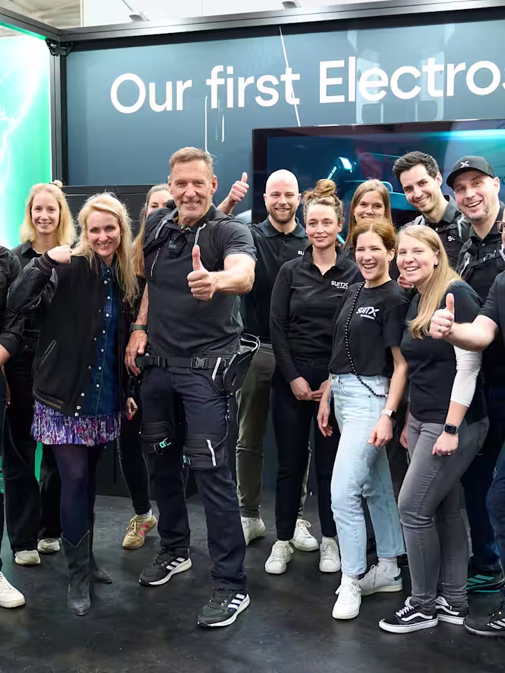 Eine Gruppe Menschen und Ralf Möller präsentieren den Hannover Messe Stand von SUITX by Ottobock.