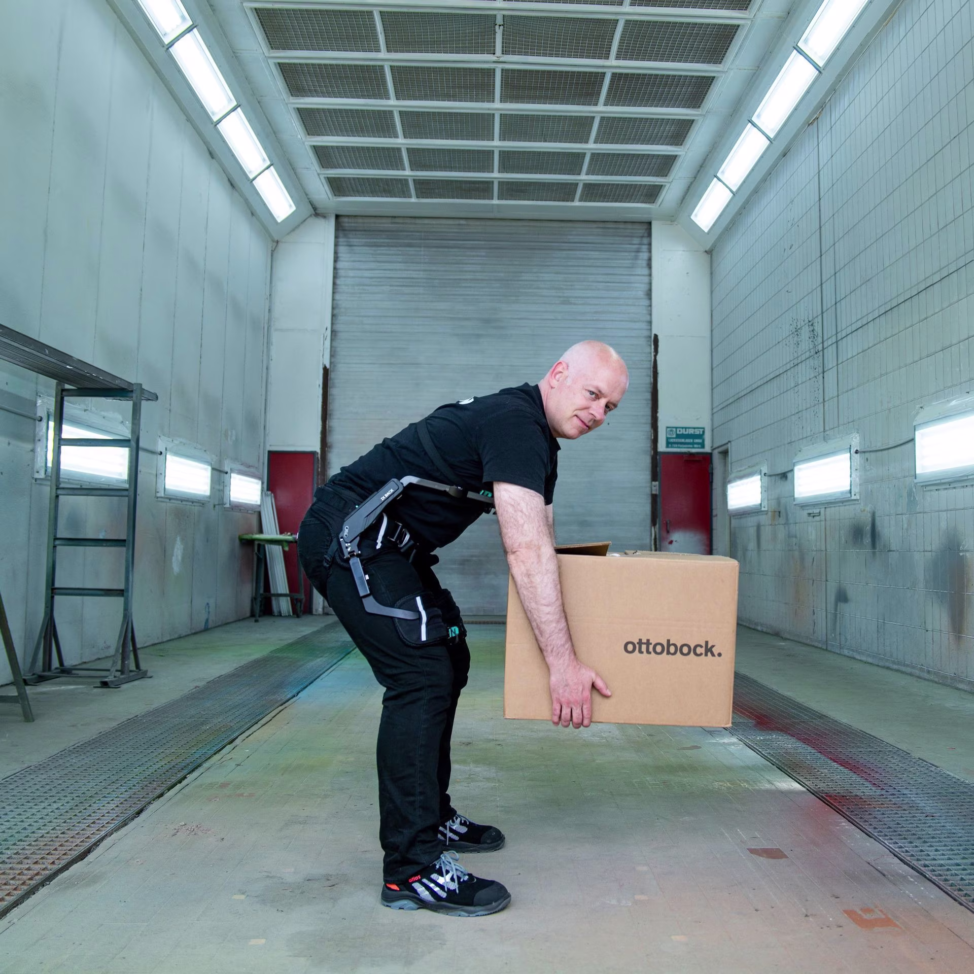 A mechanic stands in an empty hall and lifts a large package.