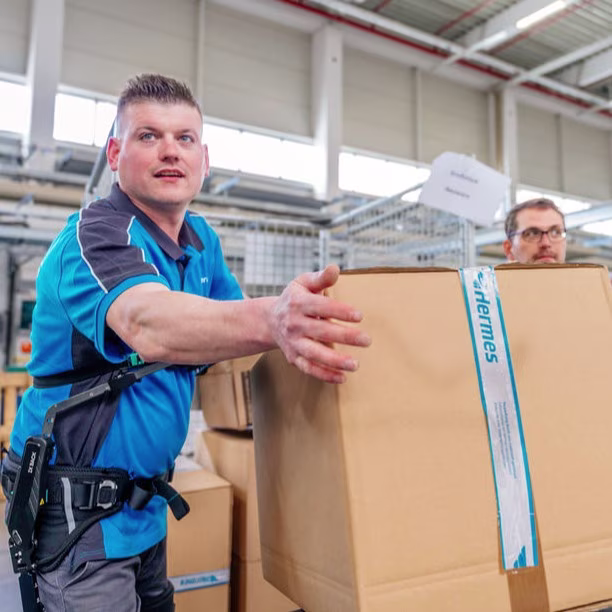 A man wearing a back exoskeleton is lifting a package.