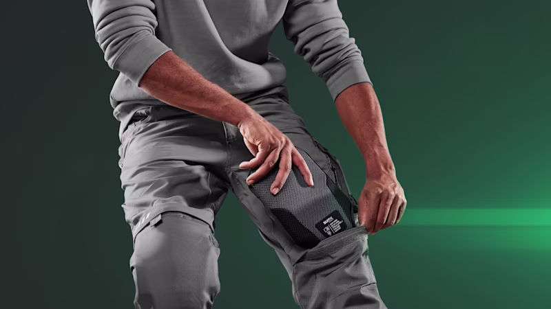 Teilansicht eines Mannes vor dunkelgrünem Hintergrund, der ein Kniepolster CX SOFT KNEE in die dafür vorgesehene Tasche seiner Arbeitshose steckt.