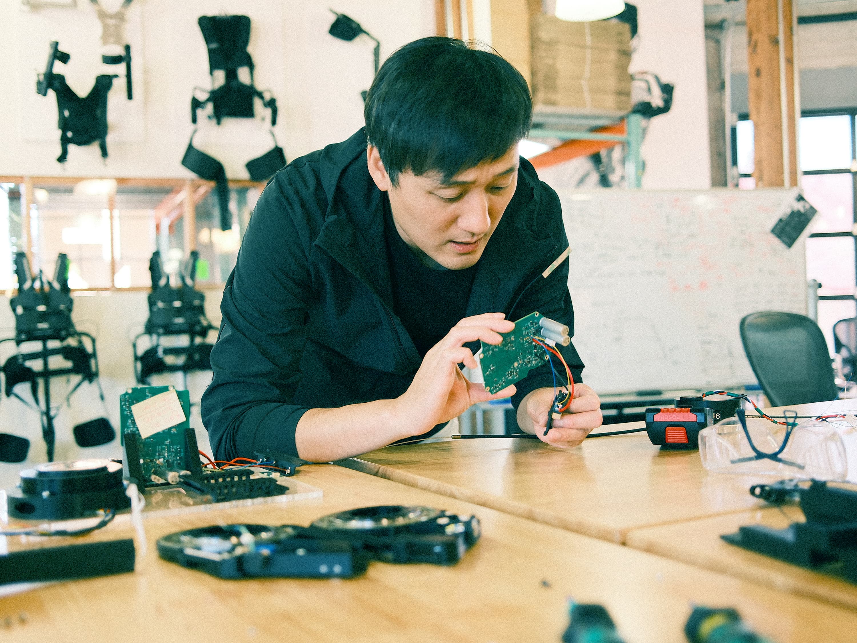 Entwickler Wayne lehnt an einem Werktisch und untersucht eine elektronische Platine.