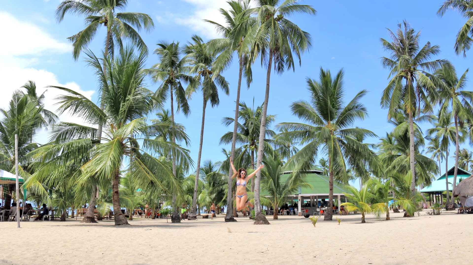 Deanna jumping on the sand on Cowrie island surrounded by tall palm trees