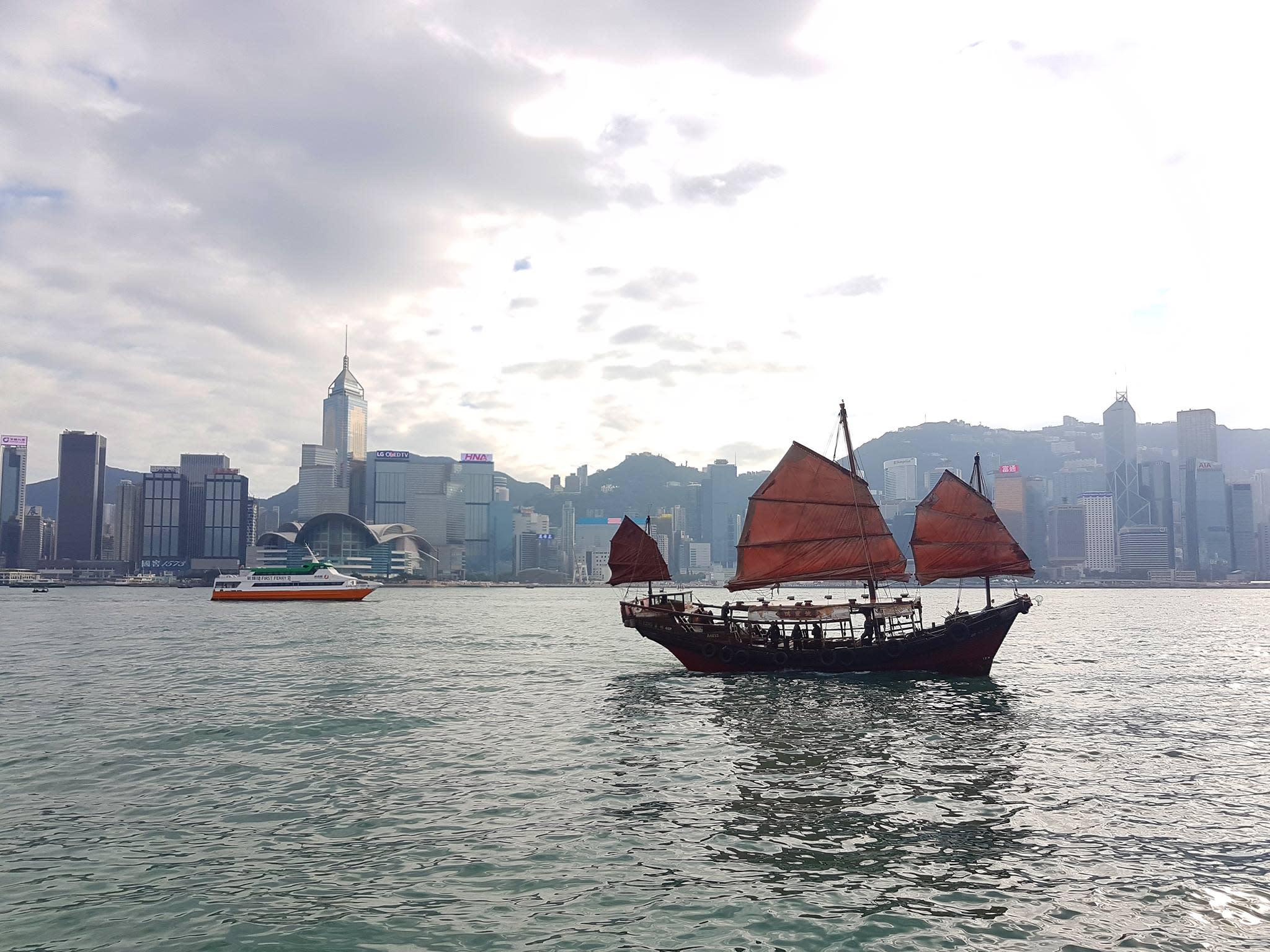Photo of an old sailboat on the water with the Hong Kong skyline in the background