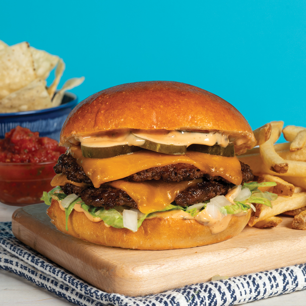 Platter with Burger and fries. Glass of pop. A bowl of tortilla cips and little bowl of salsa. 