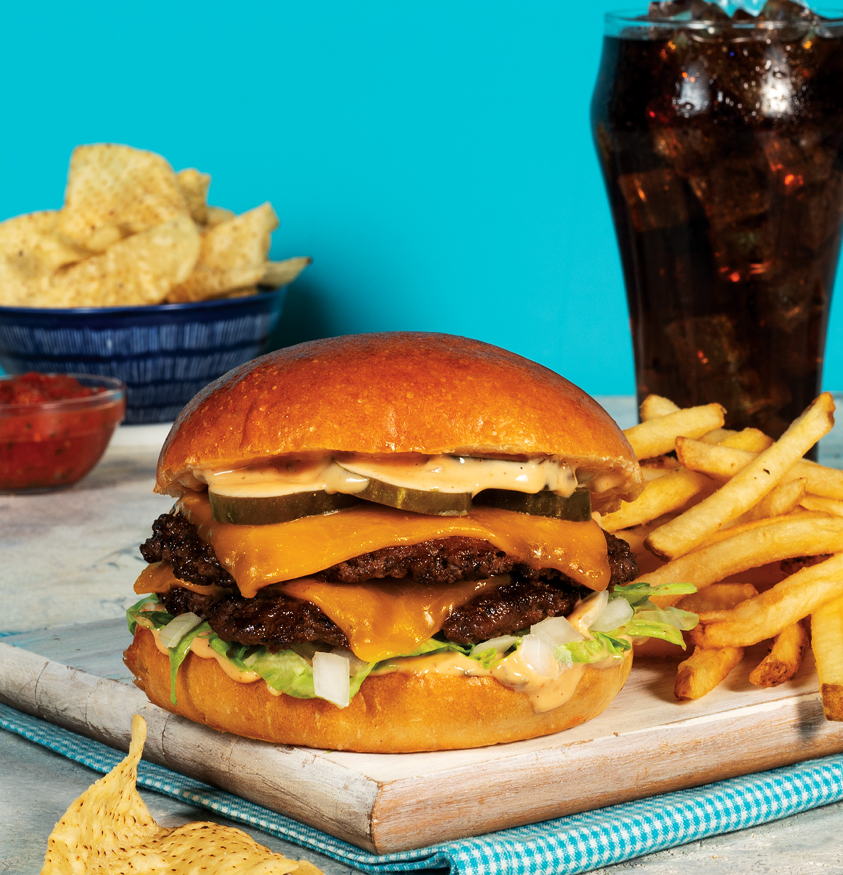 Platter with Burger and fries. Glass of pop. A bowl of tortilla cips and little bowl of salsa. 