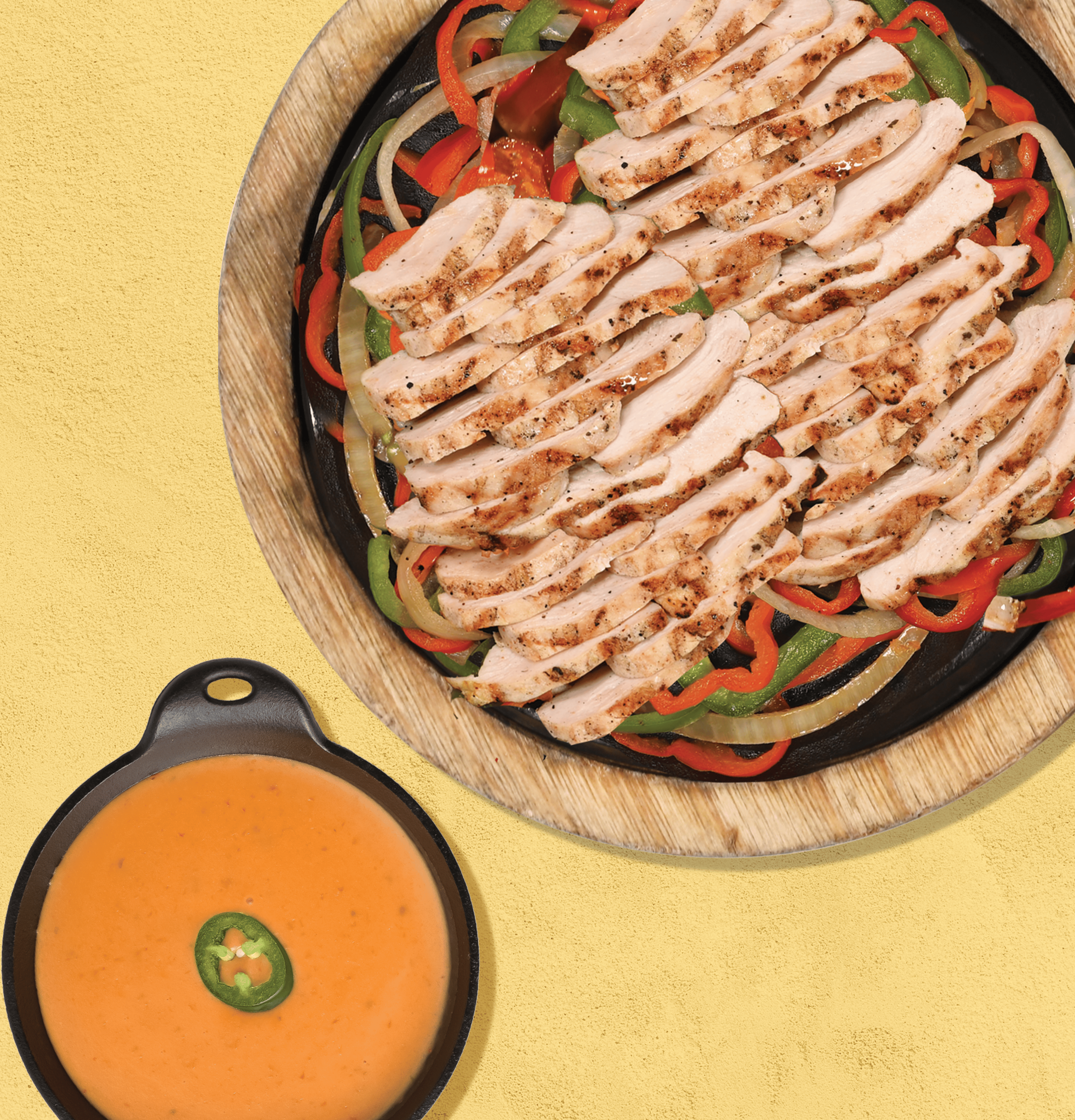 Hot plate of chciken fajita with pepper and bowl of queso cheese dip with a jalapeno slice on top