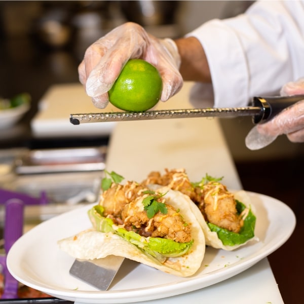 Chef zesting a lime onto fish tacos.