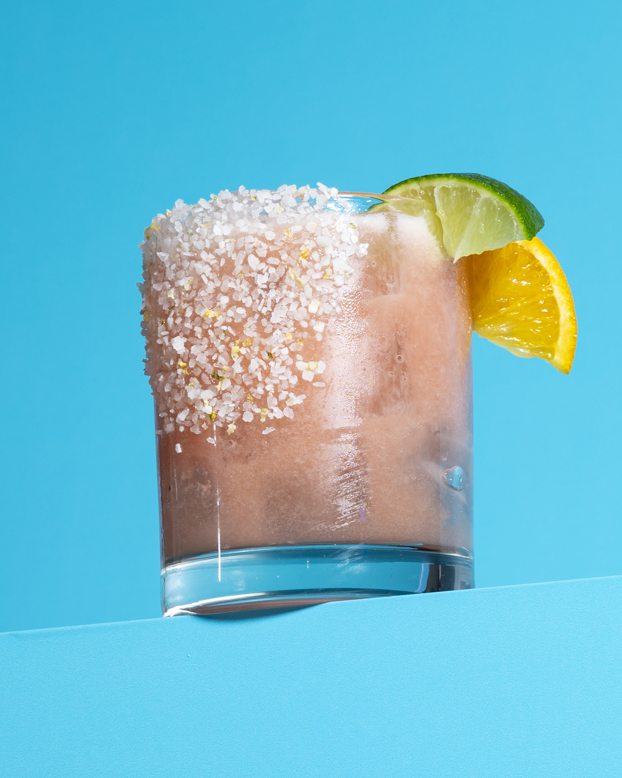 Guava shaken margarita with salt on one the left side of the glass and one lemon and one lime wedge on the right rim.
