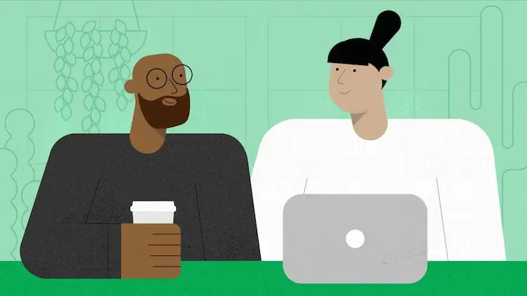 Two engineers sit side-by-side, having a conversation in front of a laptop.