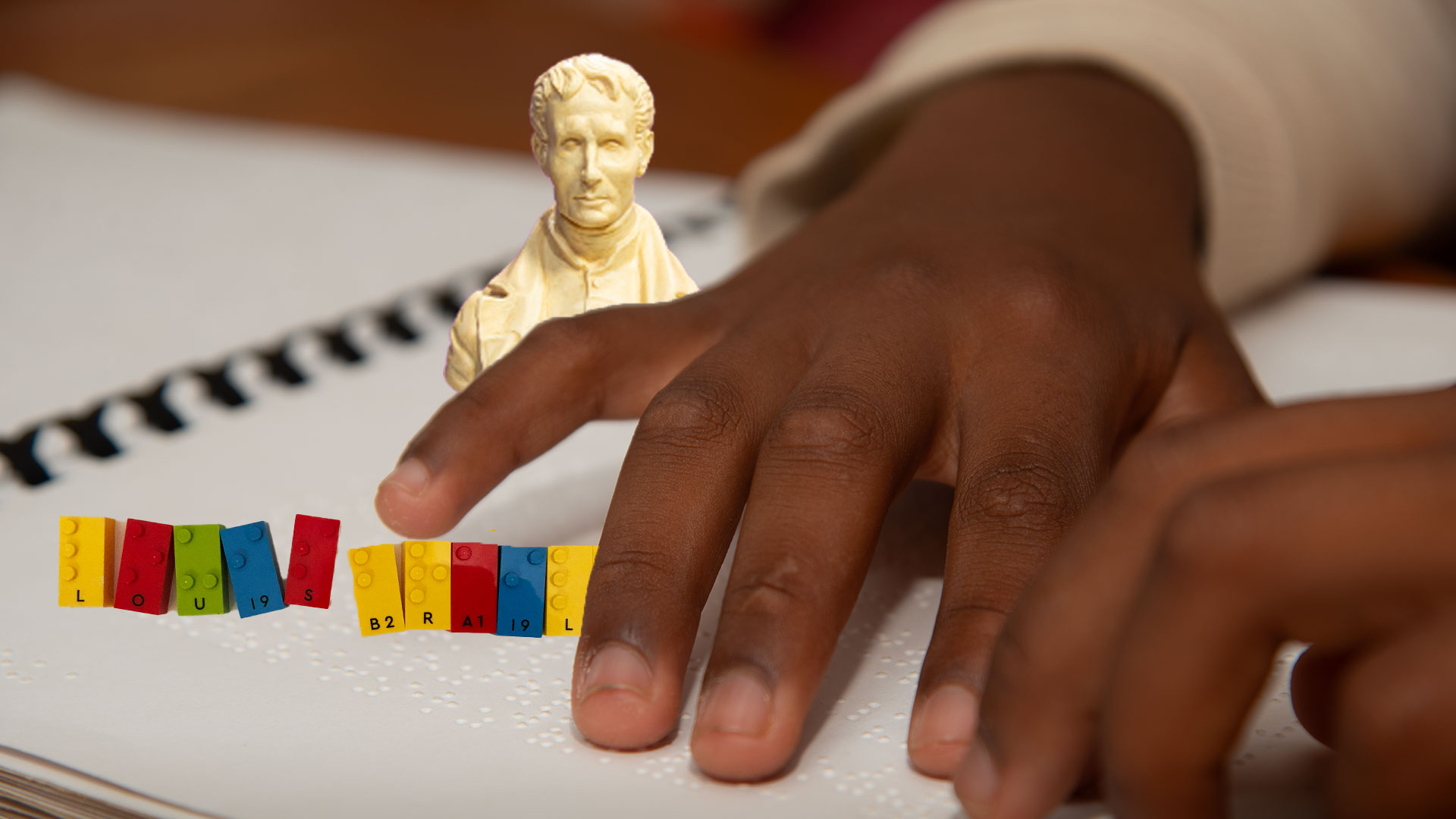 Child reading braille with LEGO Braille Bricks and a portrait of Louis Braille