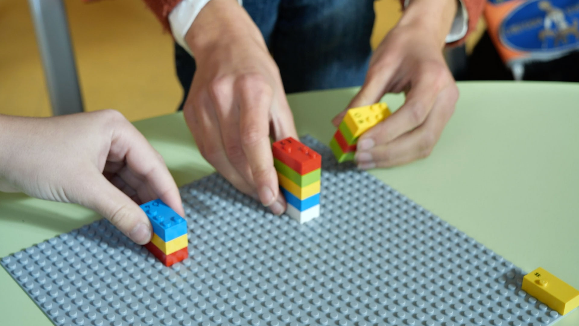 Teenagers, a girl and a boy, are playing "battle" with LEGO Braille Bricks, a numeracy activity.