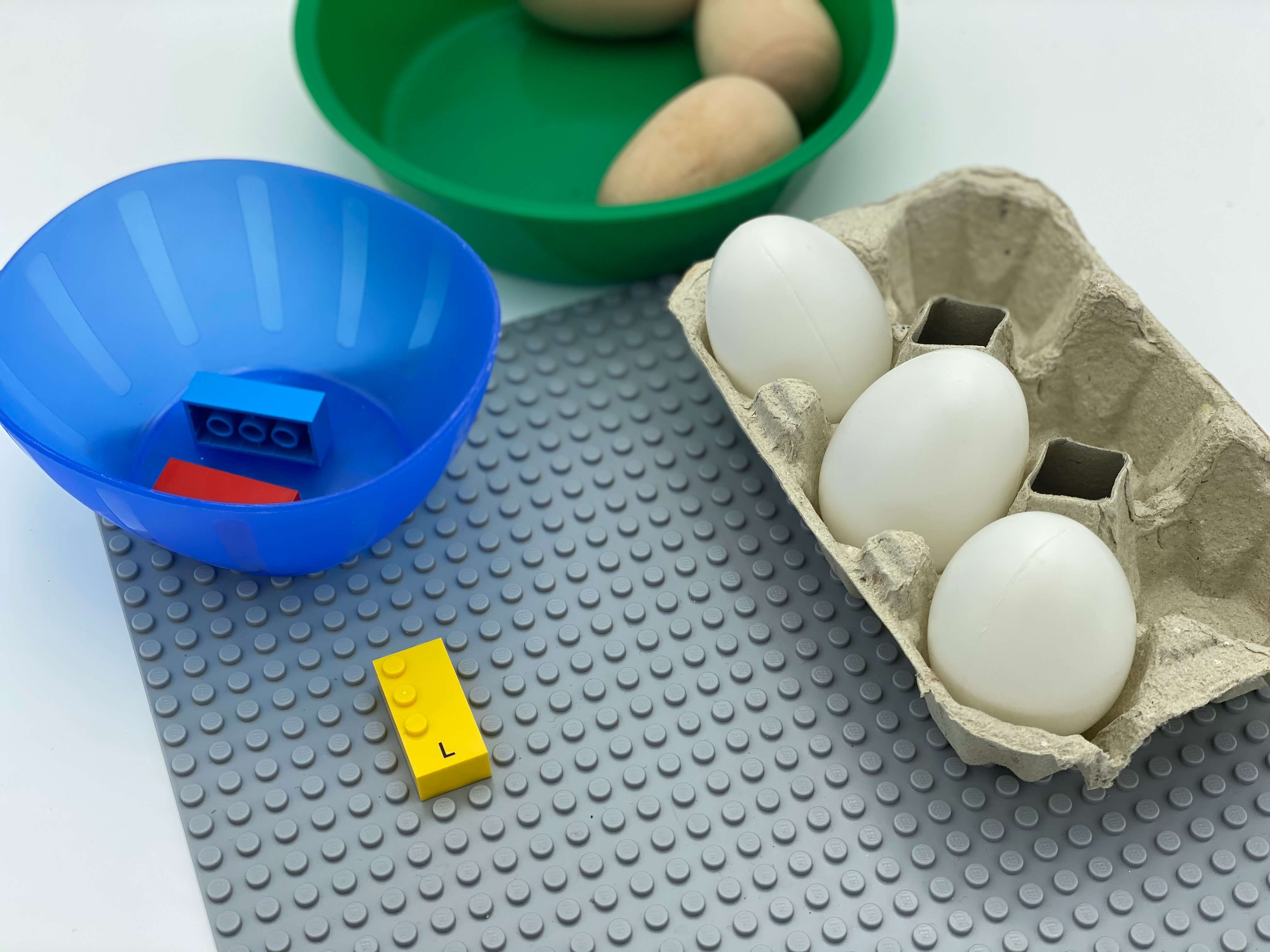 Letter brick l on the base plate, a bowl with bricks, a bowl with eggs, an egg carton with 3 eggs split in dot 1, dot 2 and dot 3.