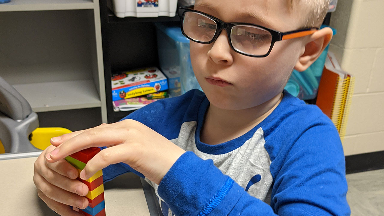 A young boy sitting at a desk, stacking LEGO bricks