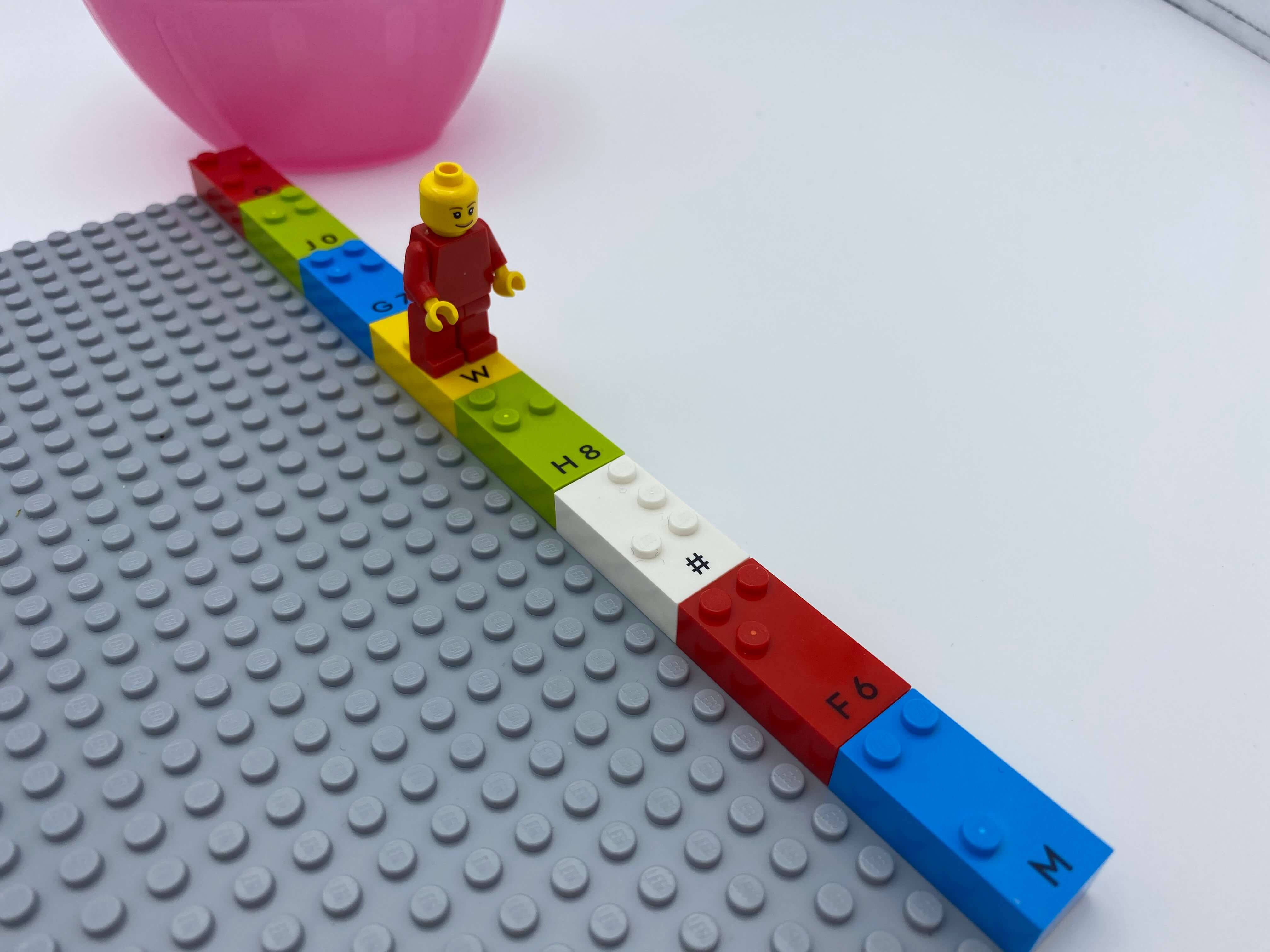 A LEGO mini figure is walking under the row of bricks.