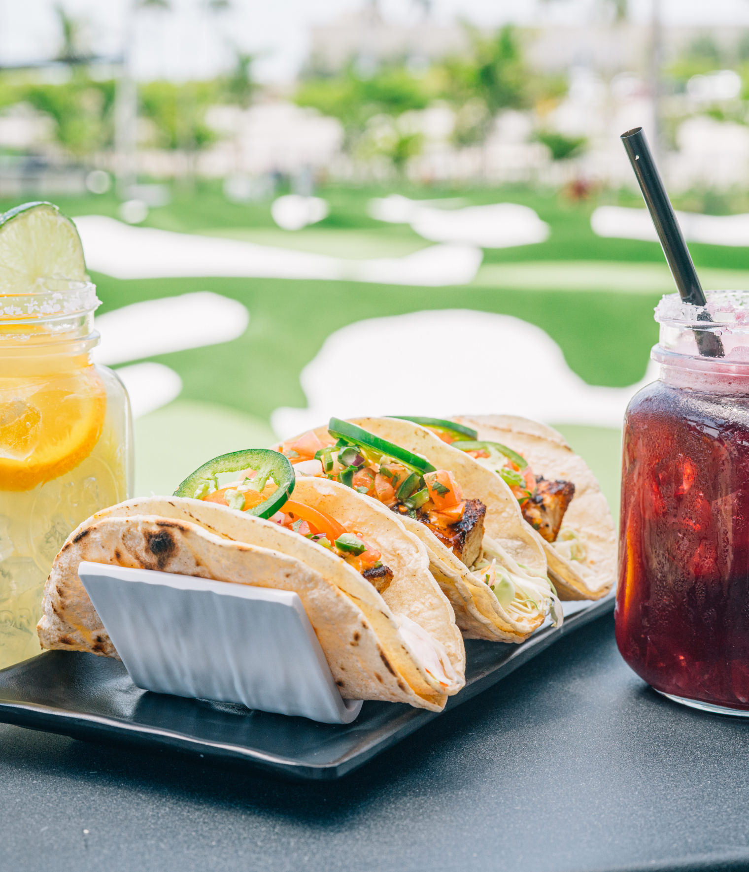 A plate of tacos and a drink on a table outdoors.