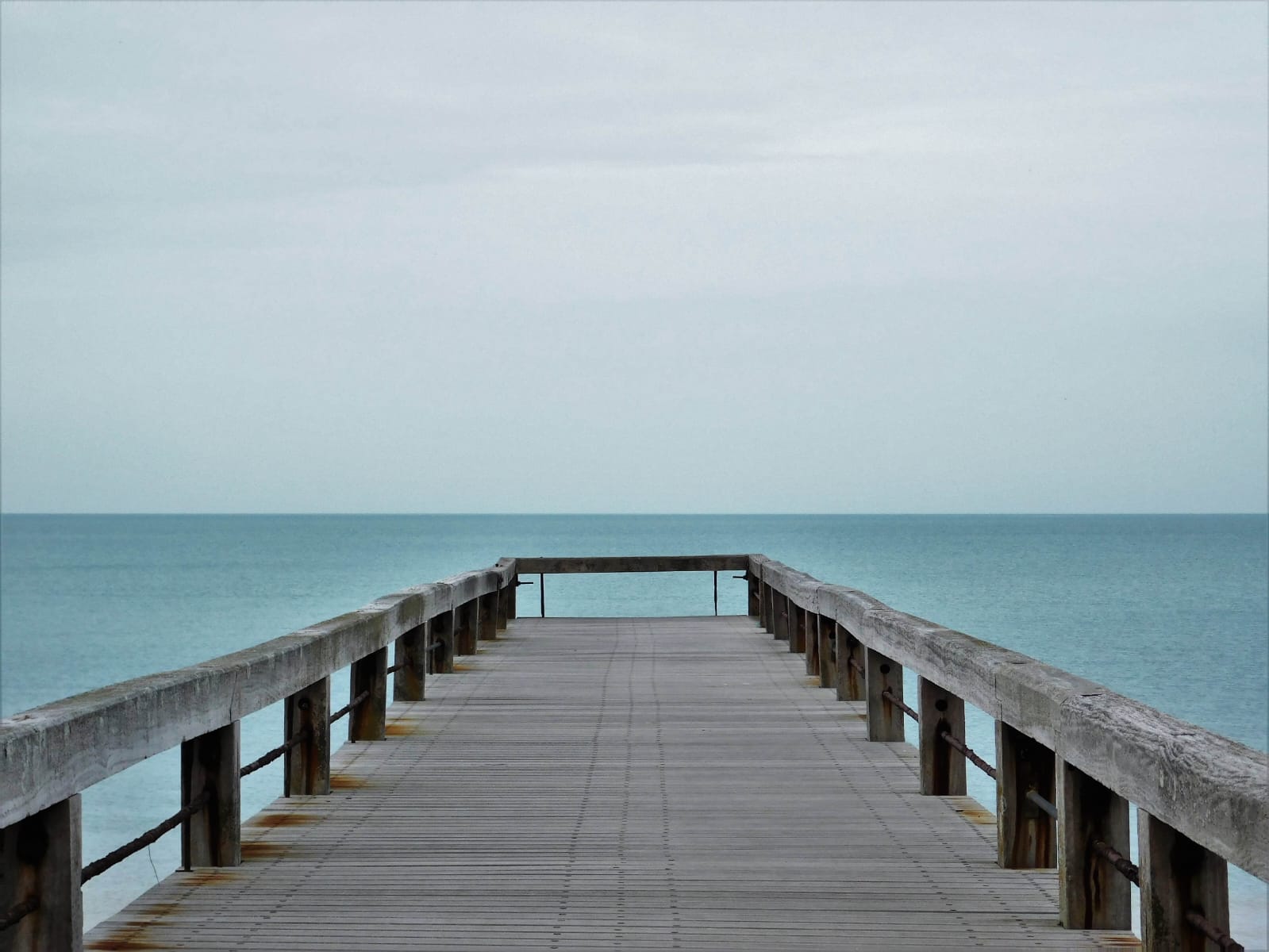 Un molo di legno che si addentra nel profondo mare blu, con il cielo azzurro sopra