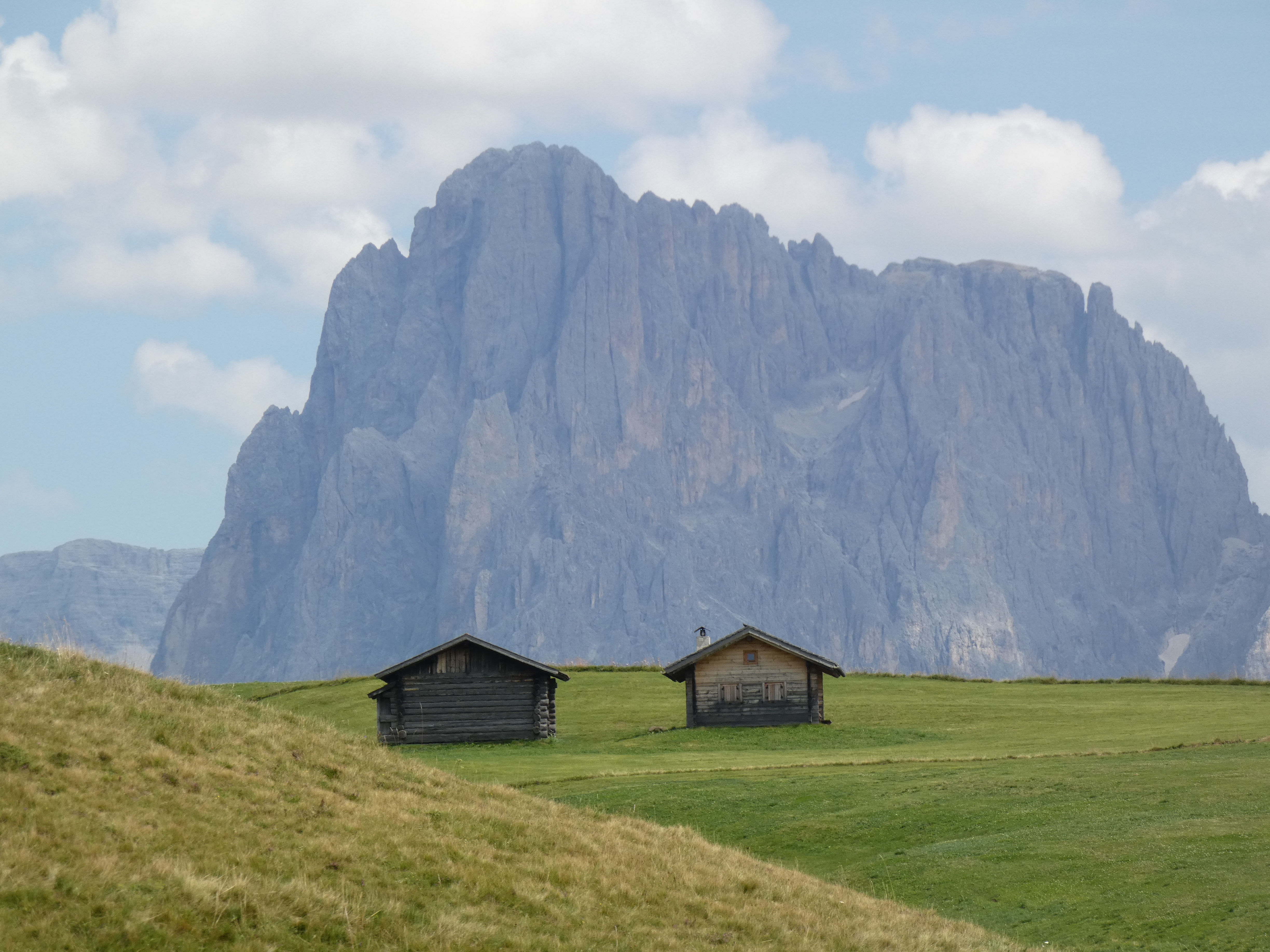 Un campo verde con due rifugi di montagna, montagne sullo sfondo