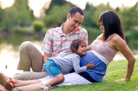 Toddler lying on pregnant mom beside dad on grass