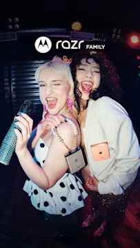 Two stylish women posing for a photo at a party, each adorned with their motorola razr phones. Text reads, “razr family.”