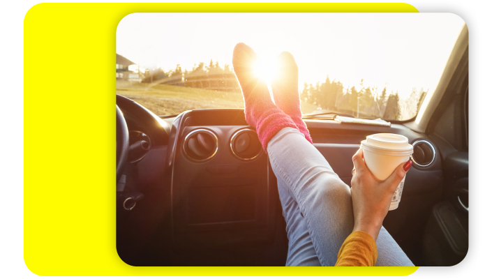 Passenger in the front seat of a car with coffee in her hand and her feet on the dashboard