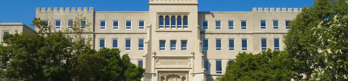 Exterior shot of Bradley Hall at Bradley University, behind several large and shady trees.