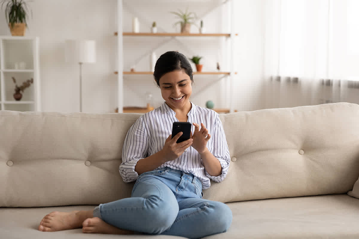 Woman on couch happily scrolling through Snapchat