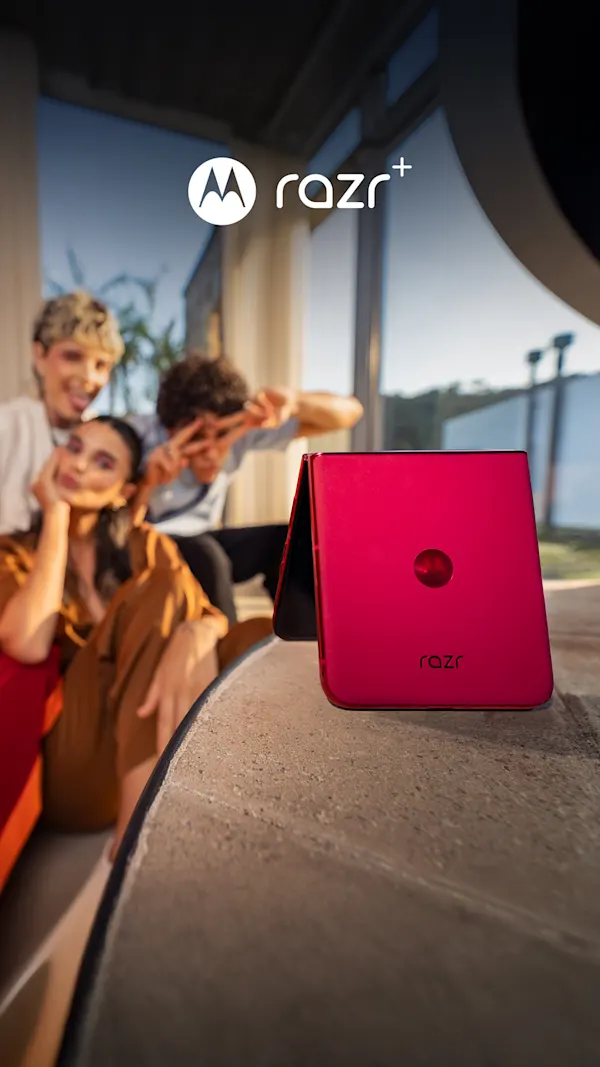 A brightly colored motorola razr phone rests on a table in the foreground, propped up to take a photo of three people in the background.