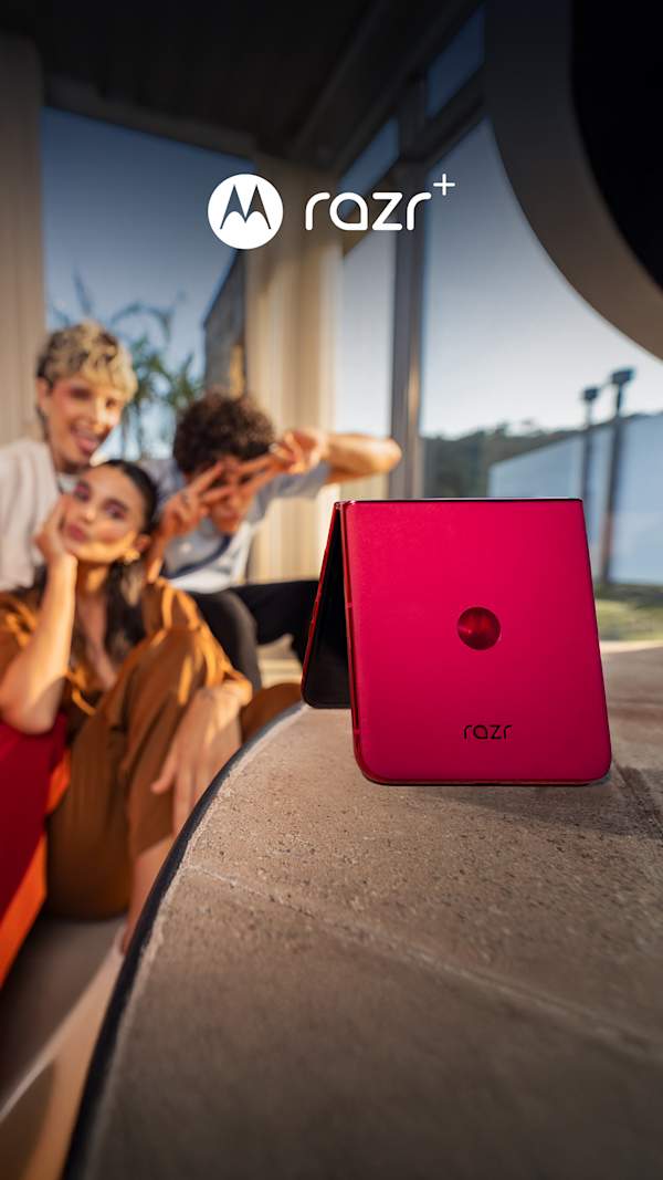 A brightly colored motorola razr phone rests on a table in the foreground, propped up to take a photo of three people in the background.