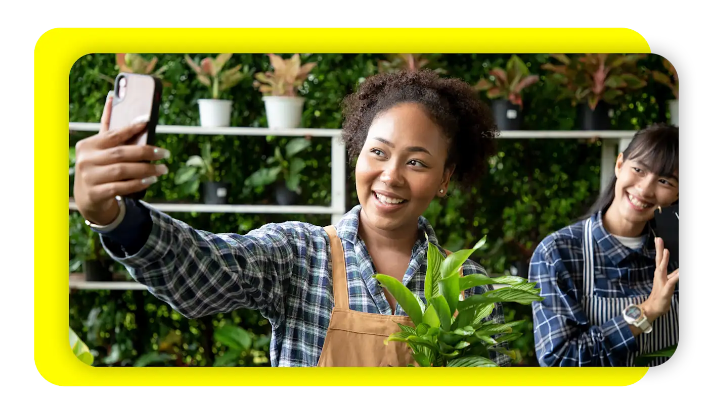 Image of two plant shop owners taking a selfie with their plants to promote their small business.