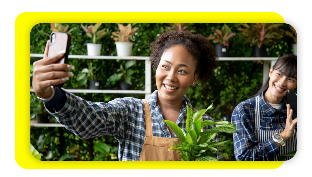 Image of two plant shop owners taking a selfie with their plants to promote their small business.