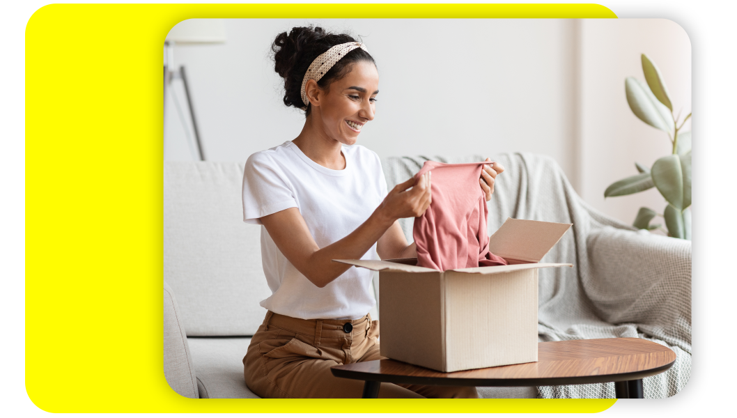 Woman holding up a pink shirt she just removed from a box