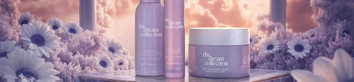 Three products from Rituals’ The Dream Collection displayed on a marble surface, surrounded by daisies and a glowing sunset sky.