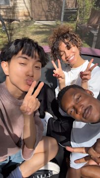 Friends smiling and taking a sunny outdoor selfie, reflecting social connection influencing insurance decisions via social media.