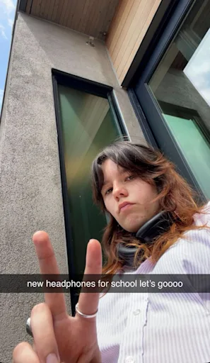 Adolescente montrant de nouveaux écouteurs dehors, geste de paix illustrant influence sociale sur achat tech.