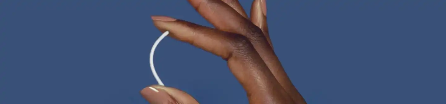 Woman’s hand holding a flexible birth control implant between her thumb and index finger.