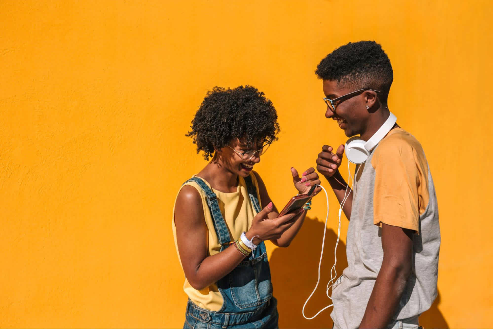 Two friends laughing together while looking at a phone, representing authentic social connection.