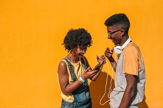 Two friends laughing together while looking at a phone, representing authentic social connection.