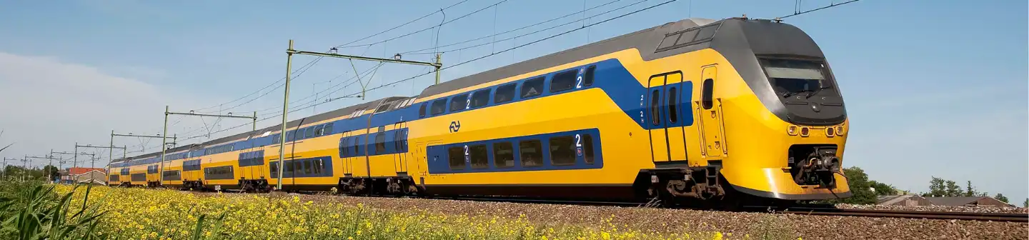 A Nederlandse Spoorwegen double-decker train travels through the countryside on an electrified railway under a clear blue sky.