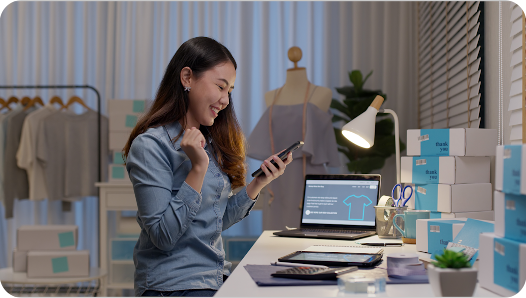 Woman working at a desk in a clothing store, smiling as she looks at her mobile phone