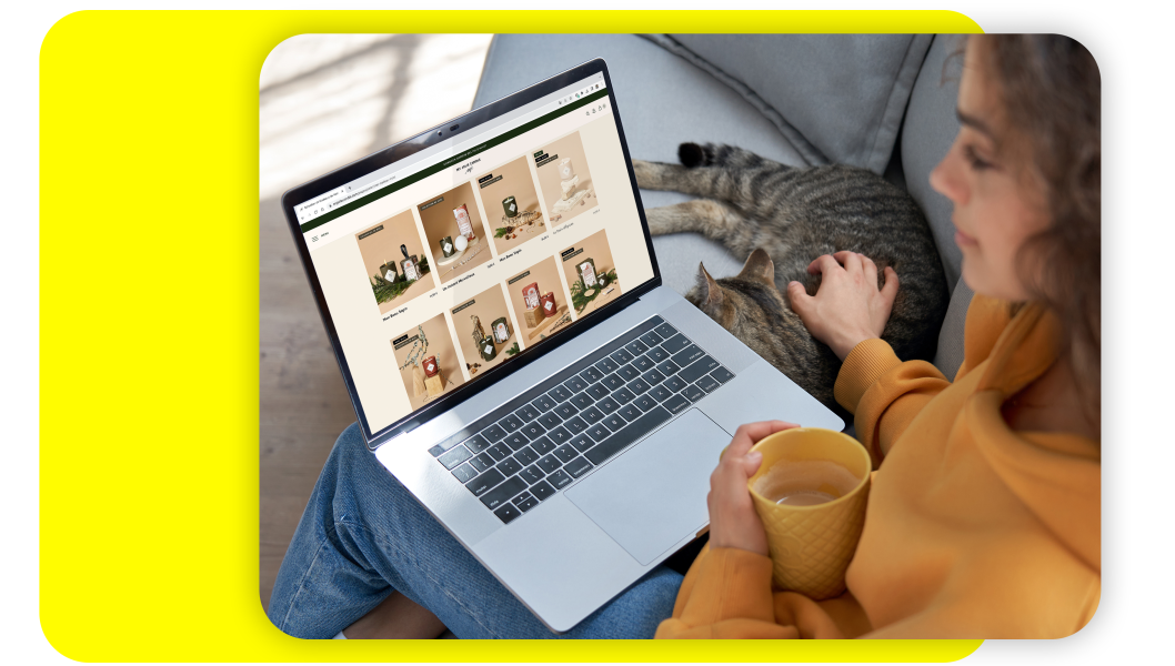 Femme faisant du shopping en ligne sur son ordinateur portable, tenant une tasse et caressant un chat