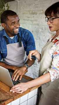 A man and a woman smiling and working together on a laptop