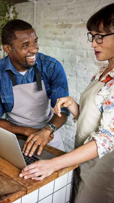 A man and a woman smiling and working together on a laptop