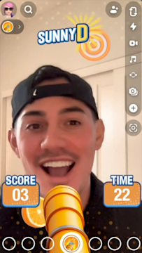 Screenshot of a young man with a backwards baseball cap playing the SunnyD Snapchat Lens game