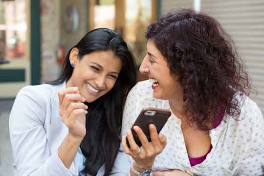 Two friends smile while scrolling phone together