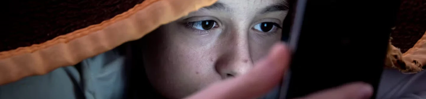 Gen Z teen looking at a phone under a blanket during a health insurance campaign on Snapchat.