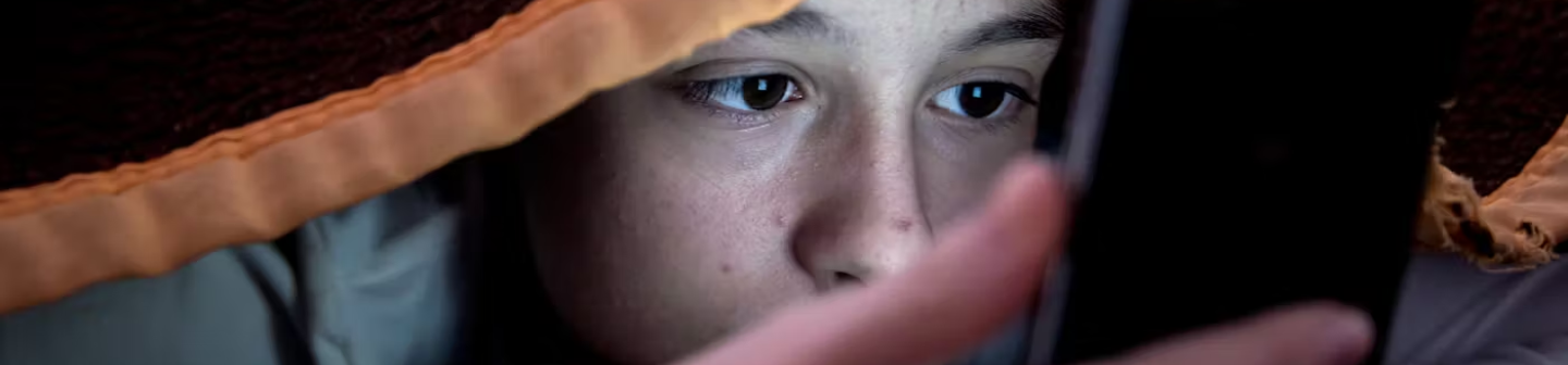 Gen Z teen looking at a phone under a blanket during a health insurance campaign on Snapchat.