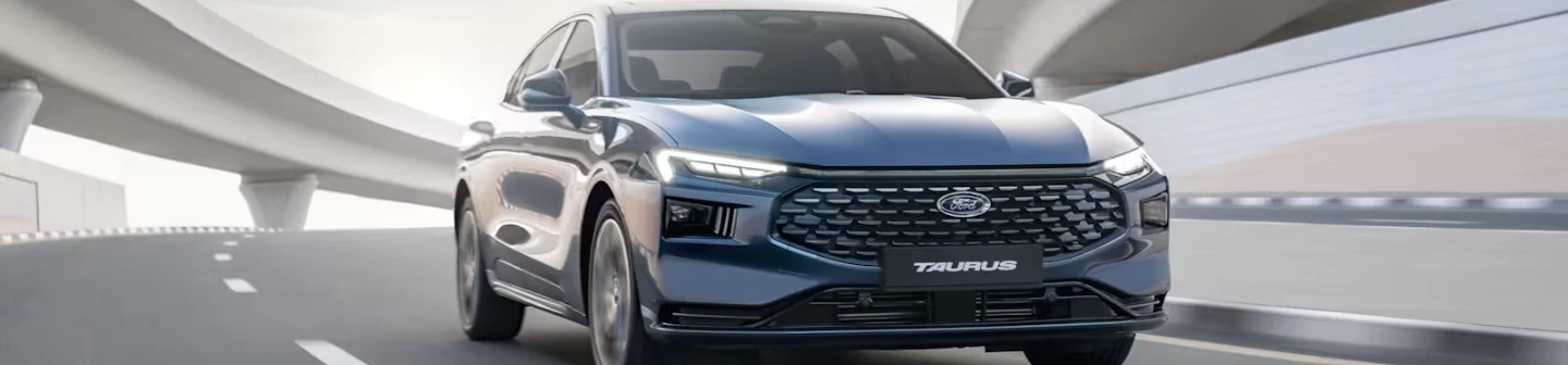 A Ford Taurus Hybrid drives along a highway, newly introduced by AJVA Ford as part of their vehicle lineup in the MENA region.