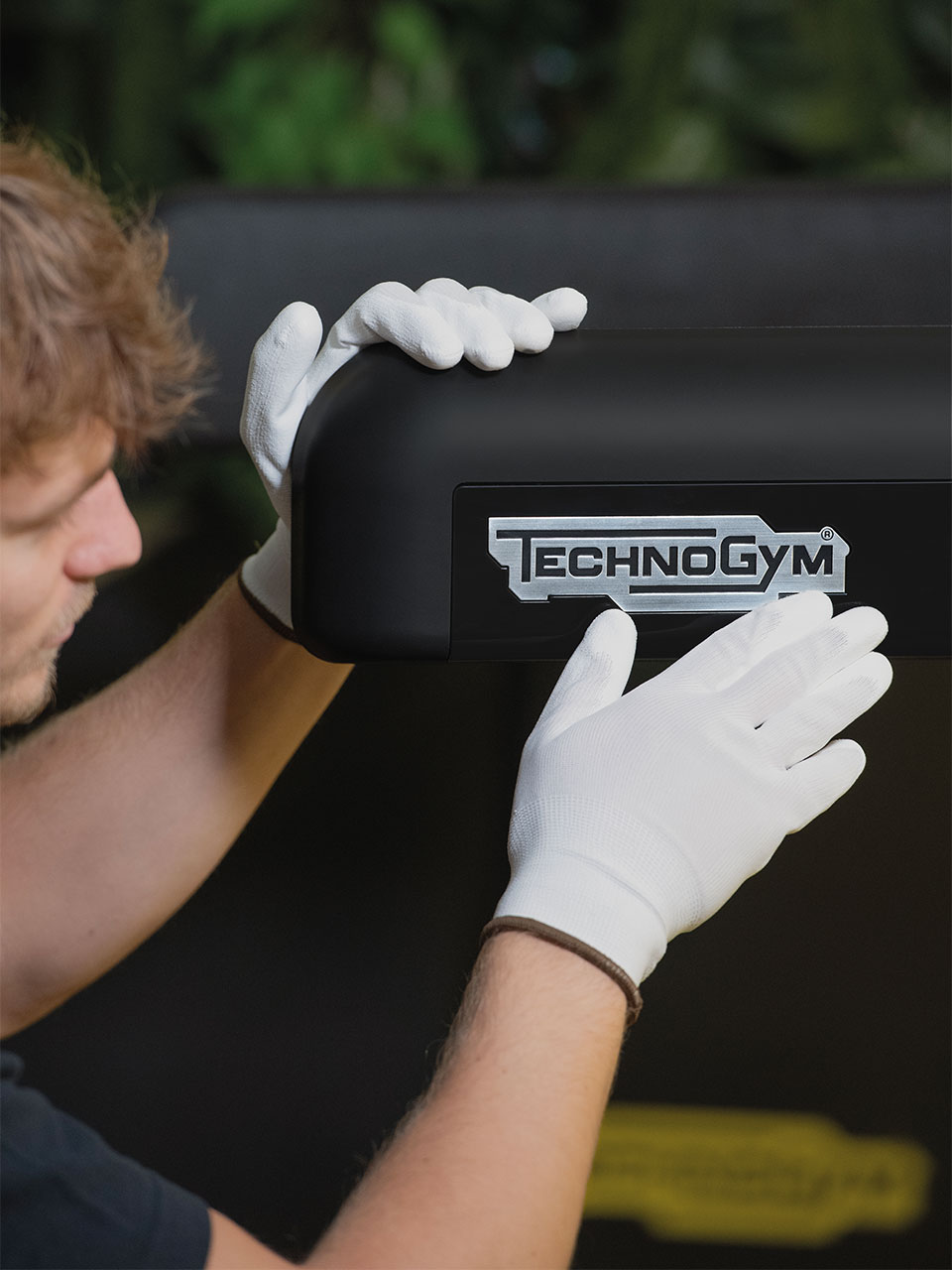 hands of a man in white gloves servicing a treadmill in need of technical assistance