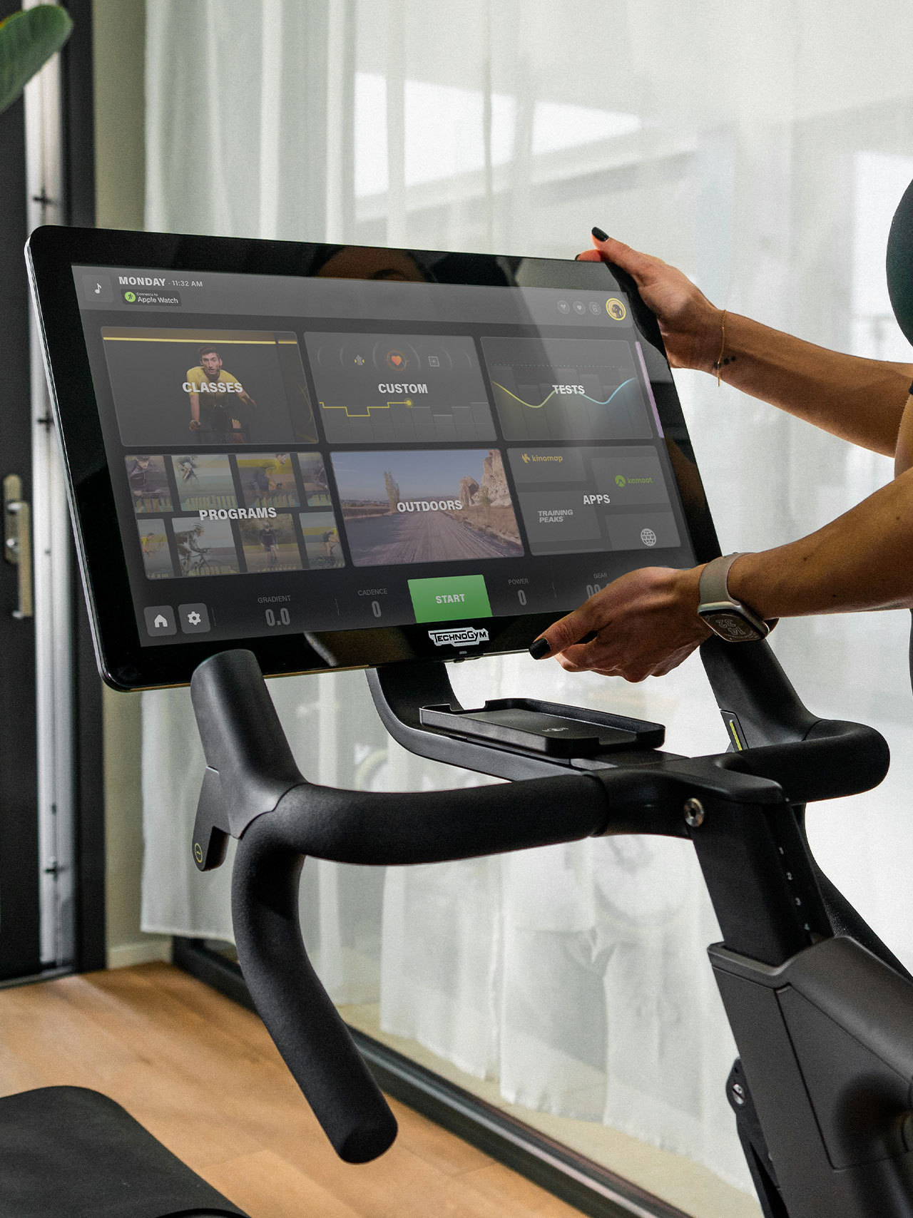 Hands of a woman adjusting the Technogym Ride indoor bike display in order to view better the training content